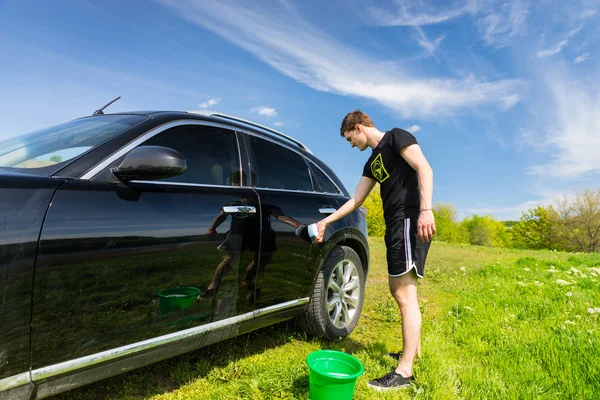 Man wassen auto in veld op zonnige dag — Stockfoto