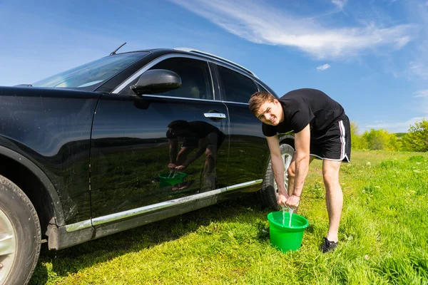 Man tvättar bilen med svamp och hink i fältet — Stockfoto