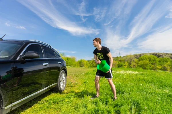 Homem que lava o carro preto no campo verde — Fotografia de Stock