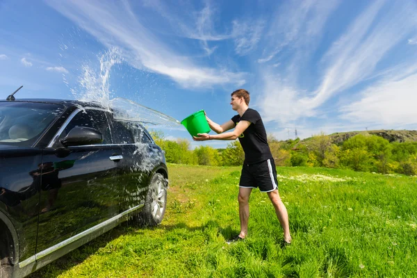 Mann wäscht schwarzes Auto im grünen Feld — Stockfoto