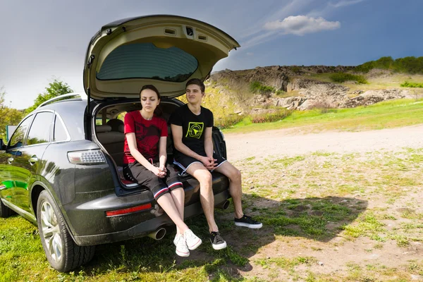 Sguing Couple Sitting on Tailgate of Car by Road — стоковое фото