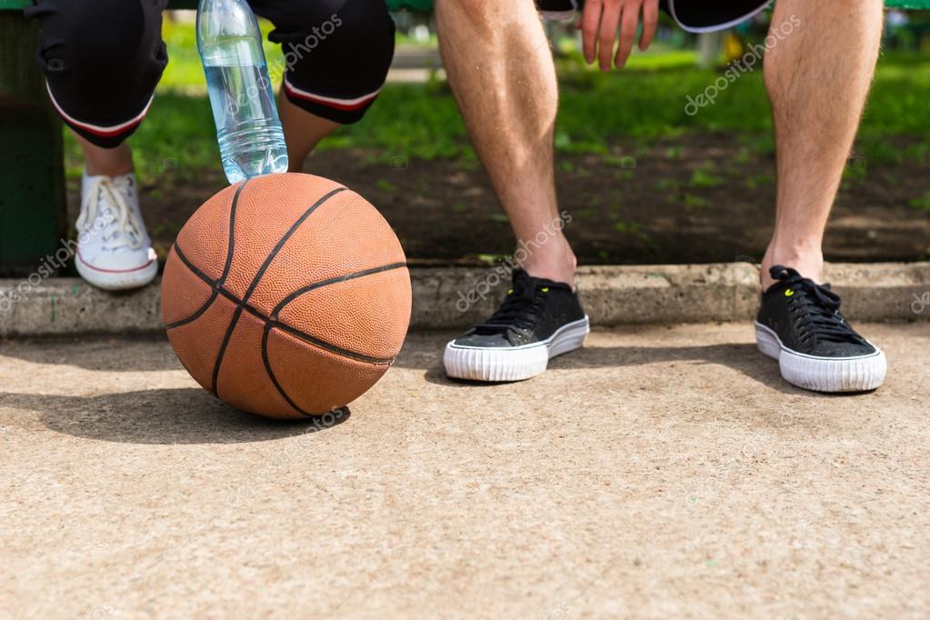 Basketball At Feet Of Couple Sitting On Park Bench Stock Photo