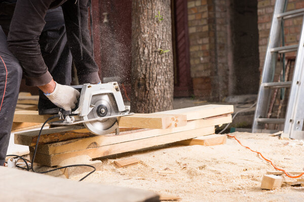 Man Using Power Saw to Cut Planks of Wood
