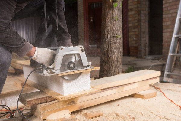 Man Using Power Saw to Cut Planks of Wood