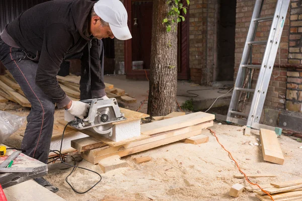 L'uomo che usa la sega elettrica per tagliare assi di legno — Foto Stock