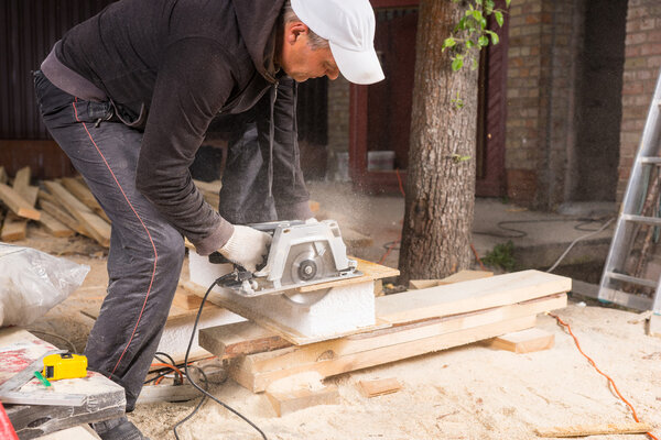 Man Using Power Saw to Cut Planks of Wood