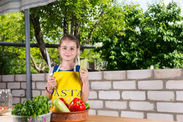 Девушка с большим ножом за столом с овощами — стоковое фото