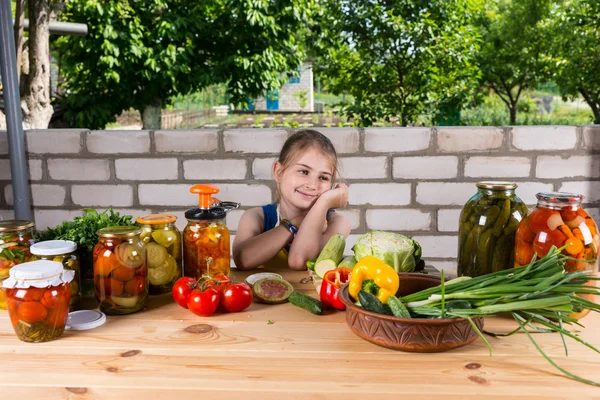 Девушка за столом, покрытая овощами и заповедниками — стоковое фото