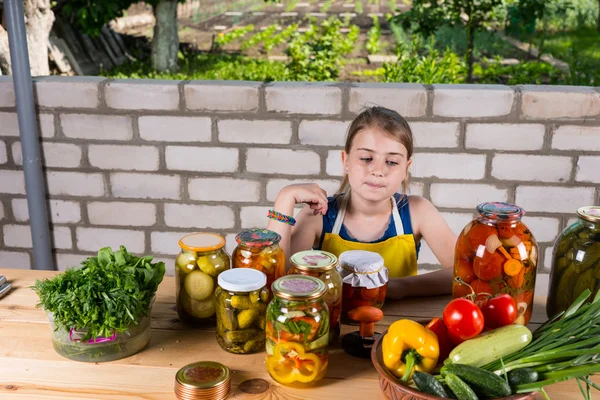 Flicka vid bordet täcks av grönsaker och konserver — Stockfoto