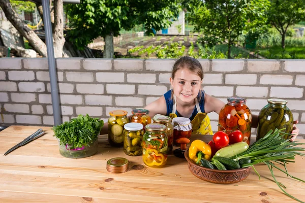 Девушка за столом, покрытая овощами и заповедниками — стоковое фото