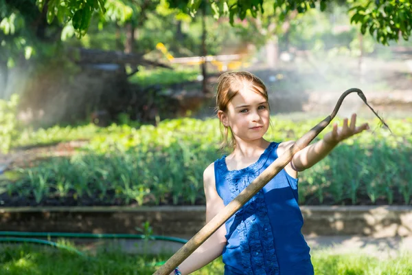 Little girl using a hoe to help in the garden — Stock Photo, Image