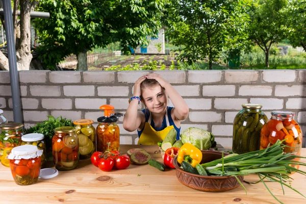 Дівчина за столом покрита овочами та консервами Стокова Картинка