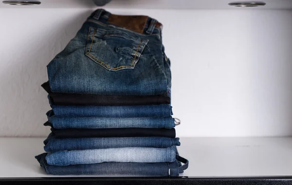 Geassorteerde Casual Jeans opgestapeld op witte plank — Stockfoto