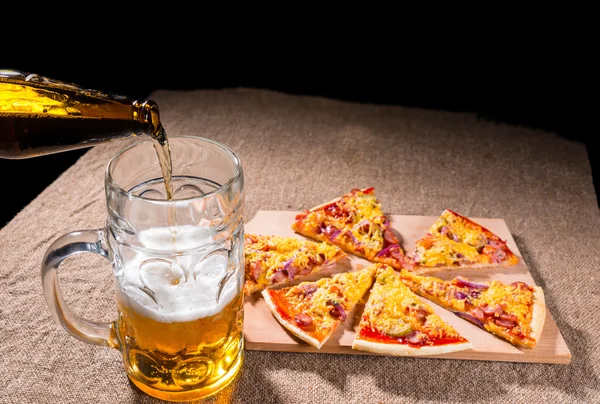 Bier gieten in glas naast Pizza segmenten — Stockfoto