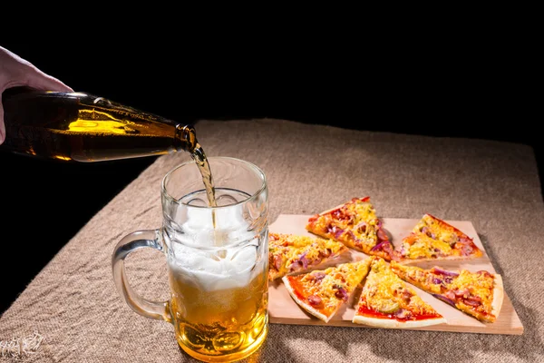 Χύνοντας μπύρα σε ποτήρι δίπλα σε φέτες πίτσ — Φωτογραφία Αρχείου