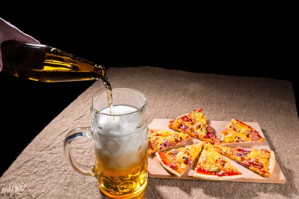 Nalewania piwa do szklanki obok plasterki pizzy — Zdjęcie stockowe
