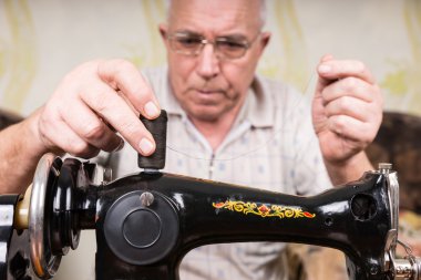 Senior Man Threading Old Fashioned Sewing Machine