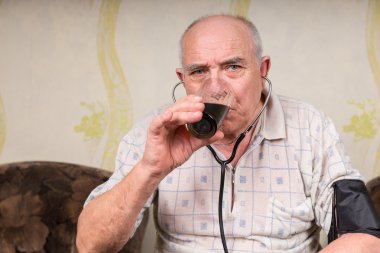 Old Man with Stethoscope Drinking a Glass of Juice