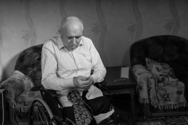 Disabled old man is trying to button his shirt