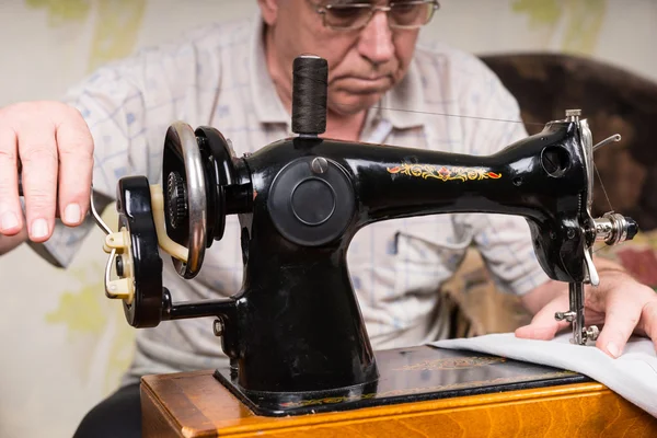 Старший человек использует старомодную швейную машину — стоковое фото