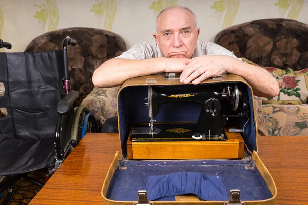 Triste gamle mand læner sig på en symaskine i en sag - Stock-foto