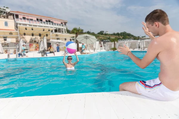 Pareja joven disfrutando en la piscina con pelota de playa — Foto de Stock