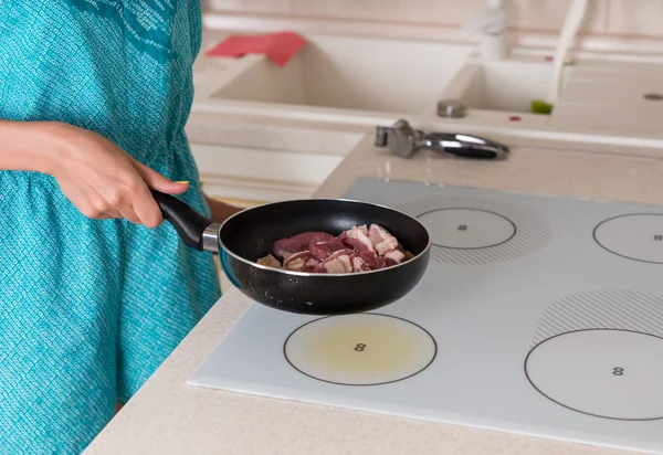 Frau legt Pfanne mit Fleisch auf Herdplatte — Stockfoto