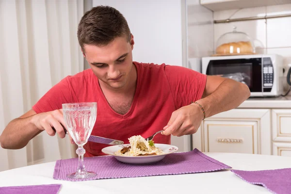 Jovem faminto come macarrão na mesa de jantar — Fotografia de Stock