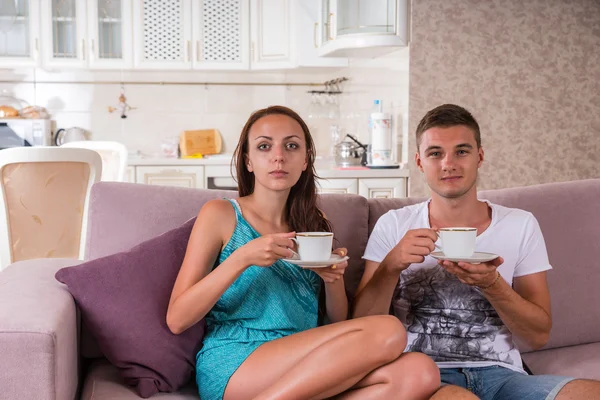 Pareja joven con café sentada en un sofá juntos —  Fotos de Stock