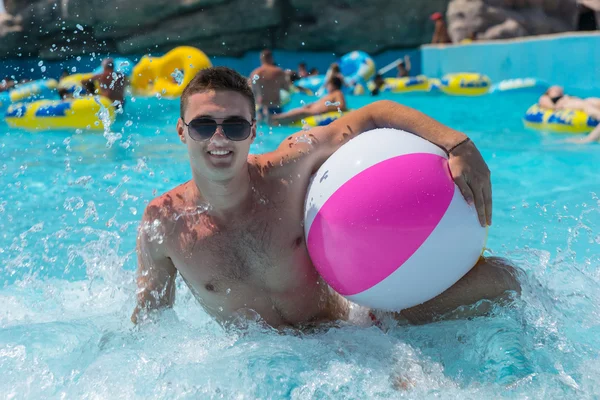 Jeune homme avec ballon de plage dans la piscine publique — Photo