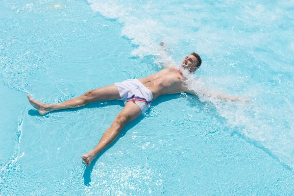 Giovane uomo sdraiato sulla schiena in onde poco profonde di piscina — Foto Stock