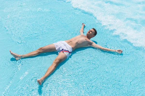 Giovane uomo sdraiato sulla schiena in onde poco profonde di piscina — Foto Stock