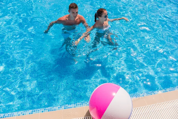 Casal jovem na piscina com bola de praia — Fotografia de Stock