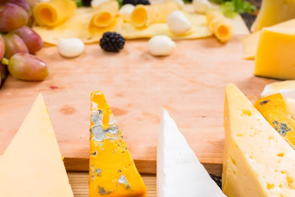 Wooden Cutting Board Surrounded by Gourmet Cheeses — Stock Photo, Image