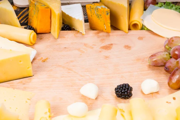 Tabla de corte de madera rodeada de quesos gourmet — Foto de Stock