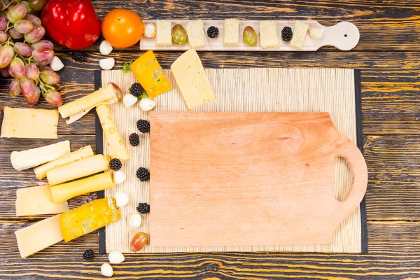 チーズと素朴なテーブルの上の果物の木の板 — ストック写真