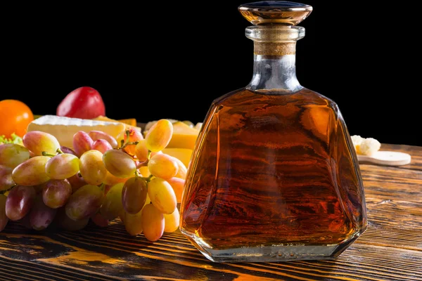 Бутылка виски на столе с сыром и виноградом — стоковое фото
