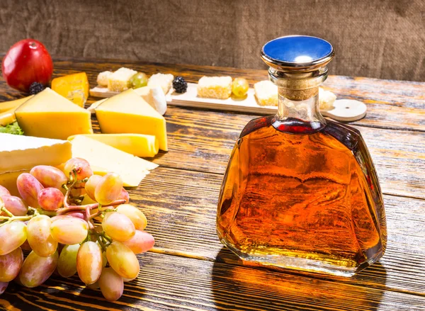 チーズとブドウを持つテーブルにウイスキーのボトル — ストック写真