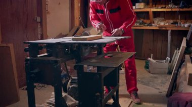 İş elbiseli bir adam atölyesinden tahta parçalar seçer..