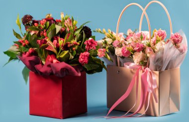 Mavi arka planda el çantası olarak stilize edilmiş sepetlerde iki çiçek aranjmanı.