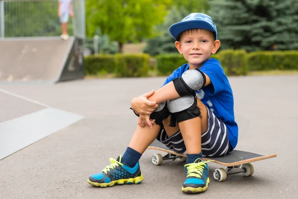 Handsome little boy sitting on his skateboard — Stock Photo, Image