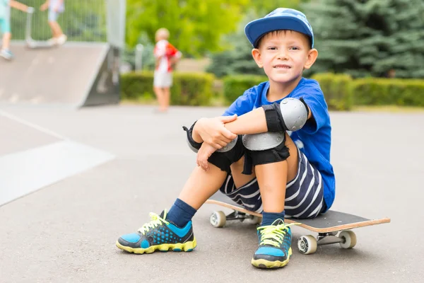 Młody chłopak siedzący na deskorolce w Skate parku — Zdjęcie stockowe