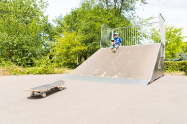 Boy Sitting on Ramp Looking Down at Skateboard