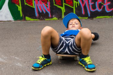 Young Boy Lying on Skateboard in Paved Lot