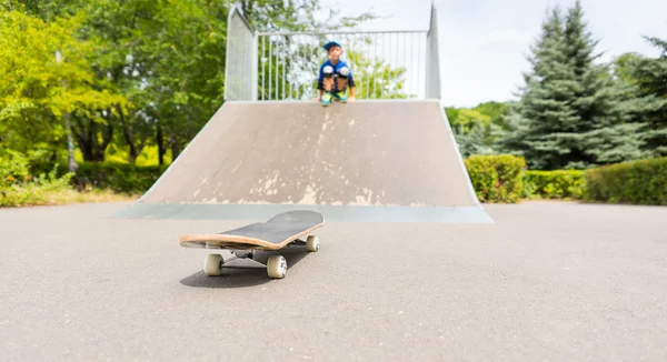 Jeune garçon sur la rampe regardant la planche à roulettes au fond — Photo