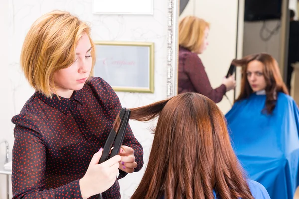 Estilista usando plancha plana para peinar el cabello de los clientes — Foto de Stock