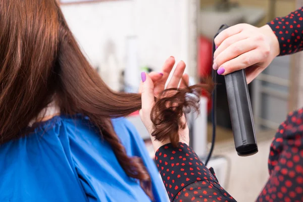 Estilista usando plancha plana en el cabello de cliente morena — Foto de Stock