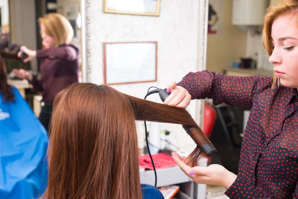 Estilista usando plancha plana en el cabello de cliente morena — Foto de Stock