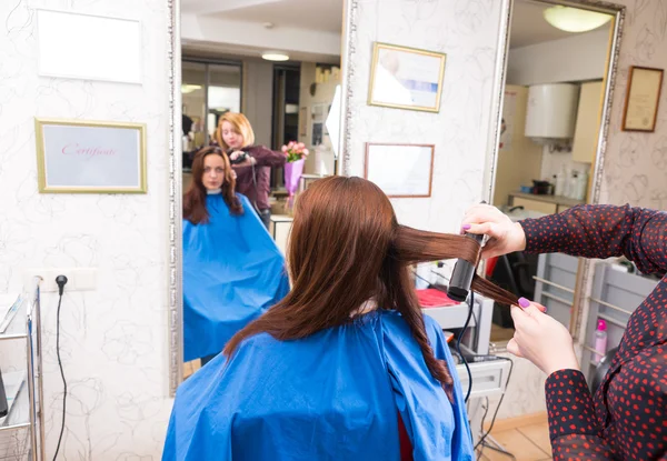 Estilista usando ferro liso no cabelo do cliente morena — Fotografia de Stock