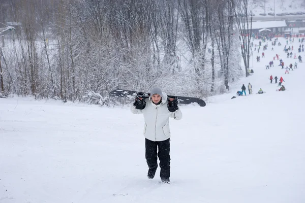 Joven caminando por la nieve con su tabla de snowboard — Foto de Stock